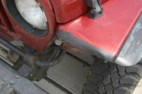 1998 Jeep TJ - Close-up of the front fender and headlight assembly on a red 1998 Jeep TJ.