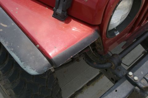 1998 Jeep TJ - Close-up of a red Jeep's front fender and headlight assembly, revealing the tire and suspension components.