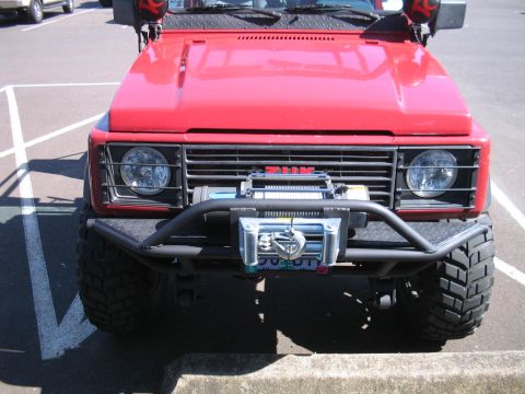 1987 Suzuki Samurai - This red SUV features a prominent winch and off-road tires, suggesting it's built for terrain.