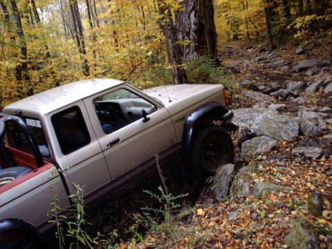 1990 Ford Ranger - A tan 1990 Ford Ranger navigates a challenging rocky path through an autumn forest.