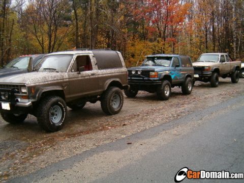 1990 Ford Ranger - A line of off-road vehicles, including a brown 1990 Ford Ranger SUV, parked on a dirt road during autumn.
