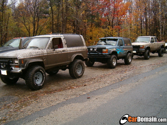Three lifted Ford Bronco II SUVs and a pickup parked on autumn forest road