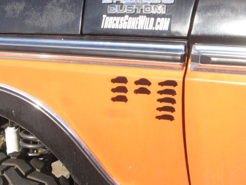 1979 Ford Bronco - The side of an orange 1979 Ford Bronco features custom decals and a series of small vehicle silhouette stickers.