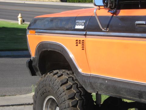 1979 Ford Bronco - Close-up of an orange and black 1978 Ford Bronco's front fender, showing its "BRONCO" badge and large off-road tire.