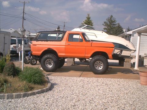 1978 Ford Bronco - Lifted 1978 Ford Bronco with oversized tires sits parked next to a boat on a trailer.
