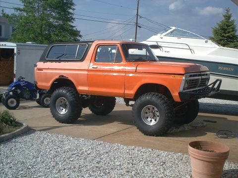 1978 Ford Bronco - Orange 1978 Ford Bronco with lifted suspension and aftermarket bumper parked on gravel next to a boat.