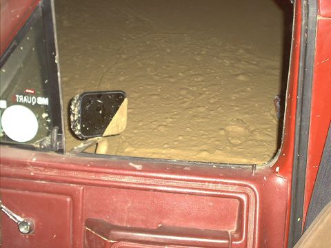 1978 Ford Bronco - View from inside a red vehicle, looking out the window at a sandy environment. The side mirror is also visible.