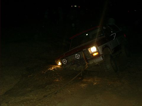 1978 Ford Bronco - A red and silver 1978 Ford Bronco is stuck in the mud at night, its headlights illuminating the challenging terrain.