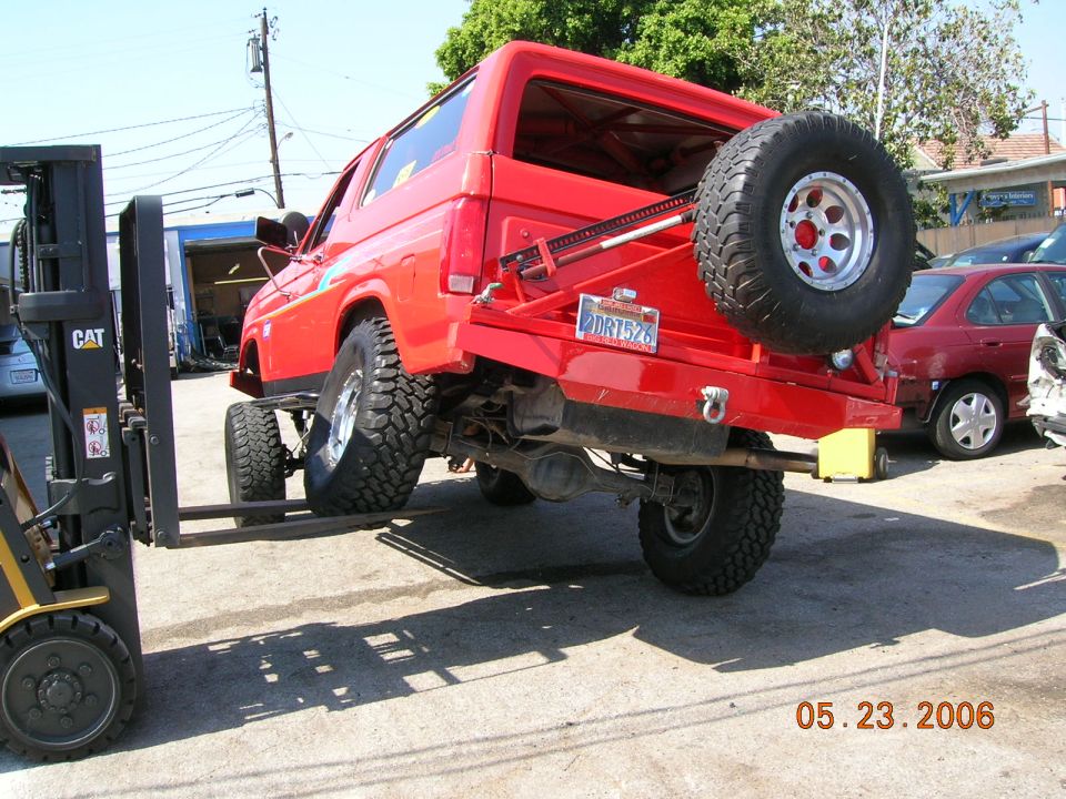 Red Ford Bronco lifted by CAT forklift at rear, showing undercarriage and spare tire