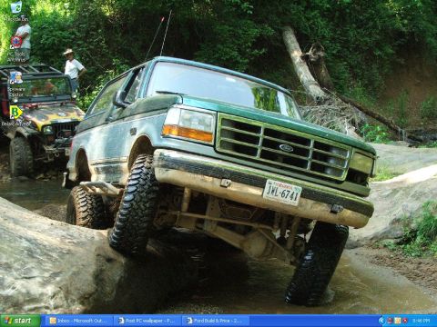 1996 Ford Bronco - Two off-road vehicles navigate a rocky stream bed surrounded by dense foliage.