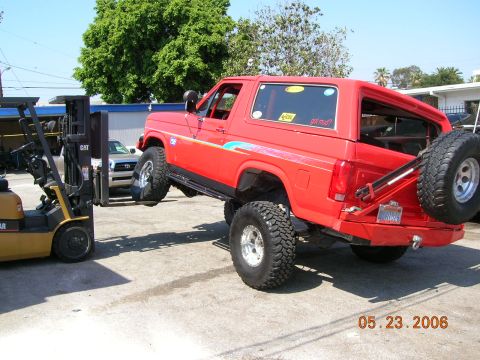 1985 Ford Bronco - A red Ford Bronco with a lifted suspension is being moved by a forklift in an outdoor lot.
