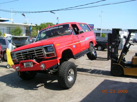 1985 Ford Bronco - A red Ford Bronco is being lifted by a forklift in an outdoor lot. The date 05.23.2006 is visible.