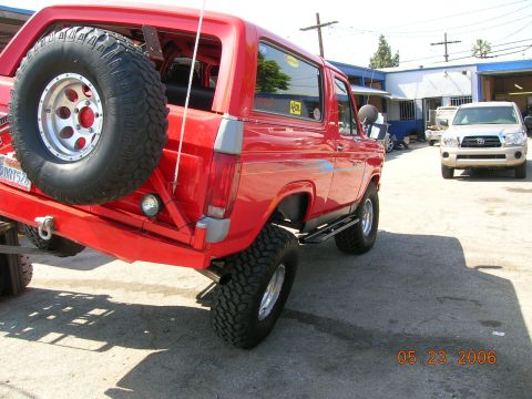 1985 Ford Bronco - A red Ford Bronco is parked outside a building, with a spare tire mounted on the rear.