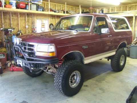 1993 Ford Bronco - A maroon 1993 Ford Bronco is parked in a garage, off-road modifications like a custom bumper and oversized tires.