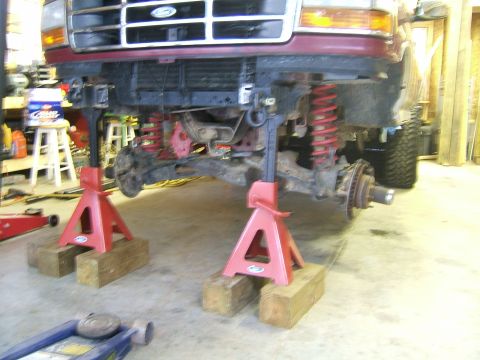 1993 Ford Bronco - Front suspension of a red Ford truck is being worked on while elevated on jack stands.