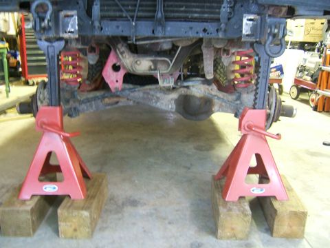 1993 Ford Bronco - Vehicle's front suspension and axle are supported by red jack stands on wooden blocks.