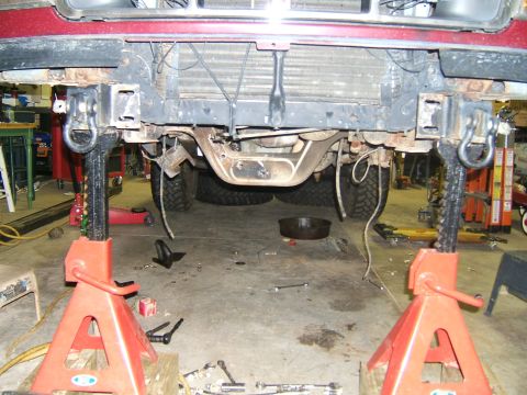1993 Ford Bronco - The front of a red vehicle is elevated on jack stands, revealing its undercarriage and suspension components.