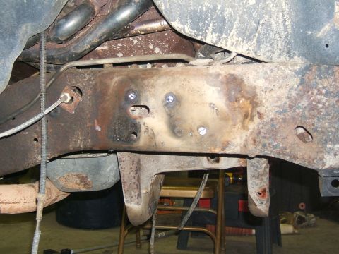 1993 Ford Bronco - Underside view of a heavily rusted vehicle frame, showing brake lines and suspension components.