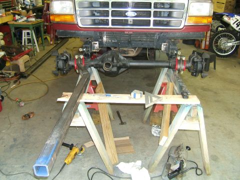 1993 Ford Bronco - Front axle assembly of a red Ford truck is suspended on sawhorses in a garage.