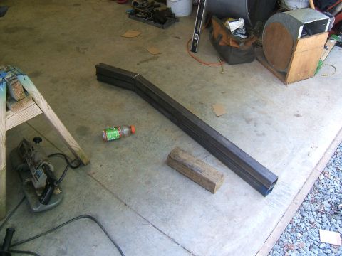 1993 Ford Bronco - A piece of bent metal tubing lies on a concrete floor next to a wooden block and a plastic bottle.