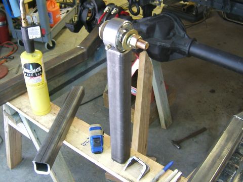 1993 Ford Bronco - A propane torch and vehicle axle assembly are shown in a workshop setting, with metal tubing and welding equipment present.