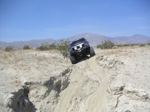 1985 Ford Bronco - Off-road vehicle navigating a challenging dirt ravine under a clear blue sky.