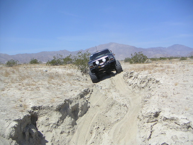 Dark lifted SUV on large tires descending a sandy desert embankment, front view