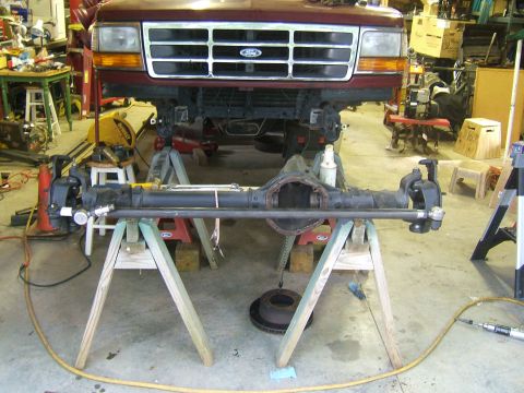 1993 Ford Bronco - The front axle assembly of a maroon Ford Bronco is removed and supported by sawhorses in a garage.