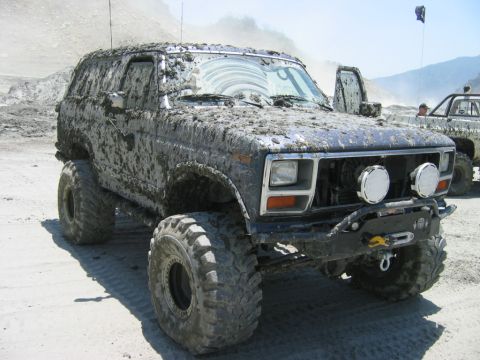 1985 Ford Bronco - This heavily modified SUV, covered in mud, has a grille design consistent with the early 1980s.