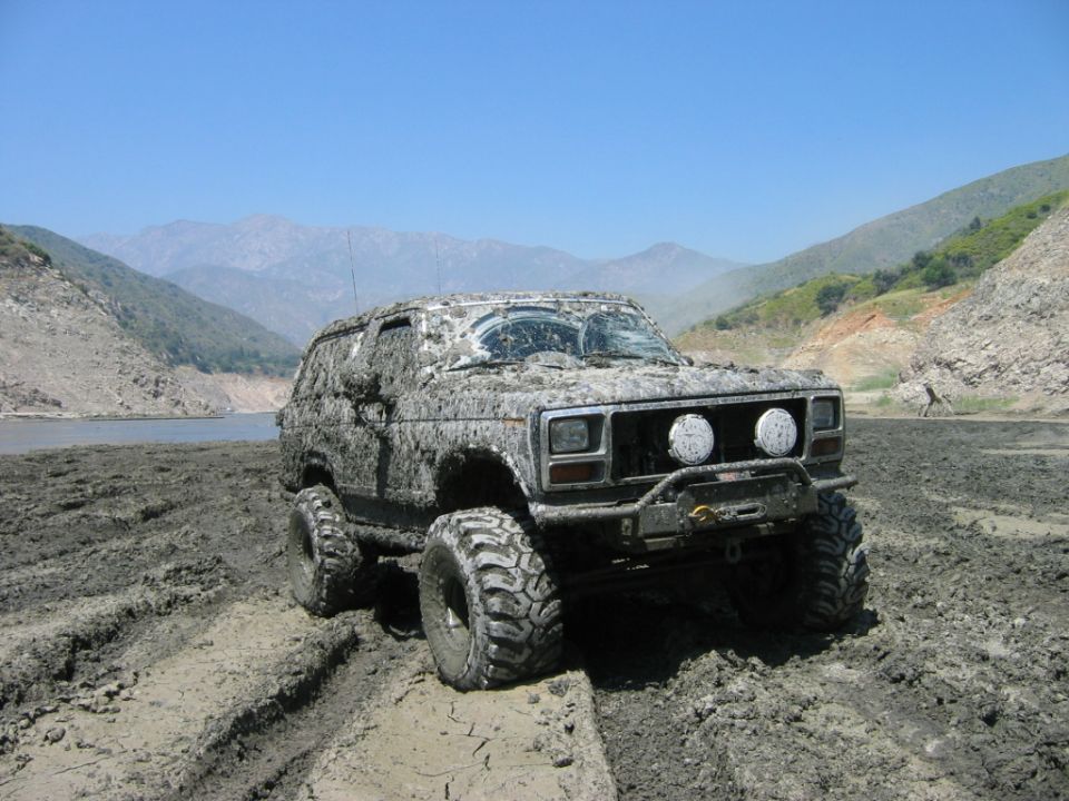Muddy lifted Ford Bronco SUV parked on cracked mud flat with mountains behind