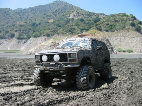 1985 Ford Bronco - Mud-covered 1985 Ford Bronco with large tires stuck in a muddy field.