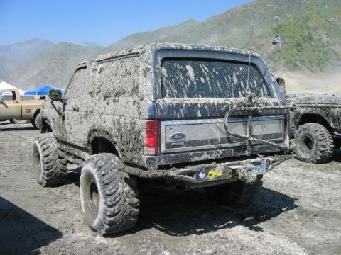 1985 Ford Bronco - This heavily mud-caked Ford Bronco is viewed from the rear, showing its large off-road tires and spare tire mount.