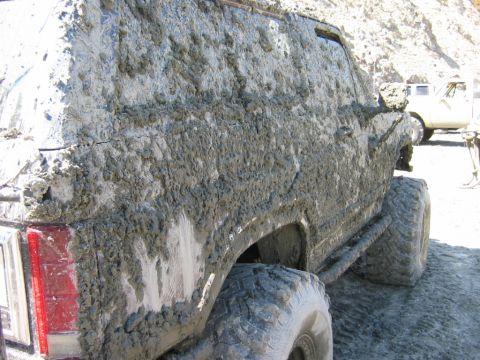 1985 Ford Bronco - This heavily mud-caked 1985 Ford Bronco shows off its off-road capabilities, with another vehicle visible in the background.