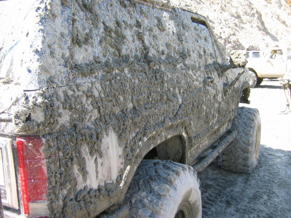 Rear side of an SUV covered in thick gray mud with a large off-road tire