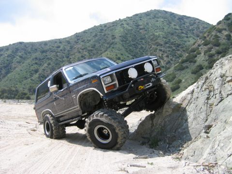 1985 Ford Bronco - This modified Ford Bronco is navigating a steep, rocky incline on a dirt trail.