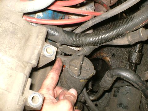1989 Ford Bronco - Close-up of an engine bay component, possibly a filter or sensor, with a hand indicating a specific area.