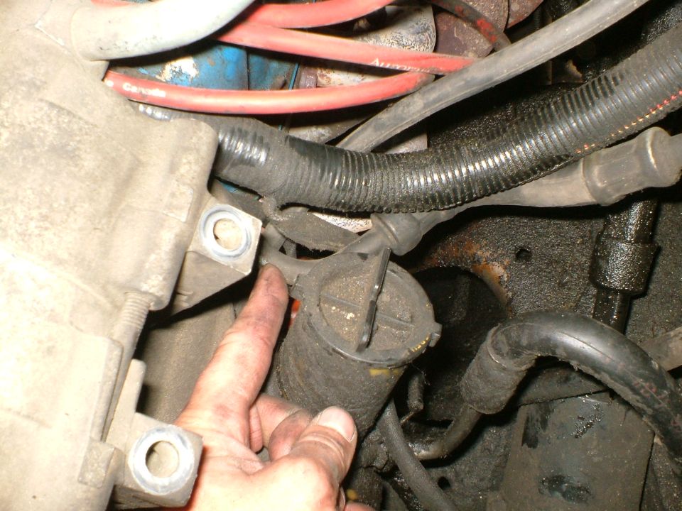 Close-up of an engine bay component with a hand pointing to it