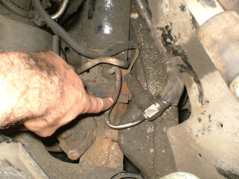 1989 Ford Bronco - Close-up view of engine bay components, including hoses and metal brackets, with a hand indicating a specific part.