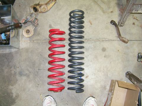 1993 Ford Bronco - Two coil springs, one red and one gray, are laid out on a concrete floor with various suspension components visible.