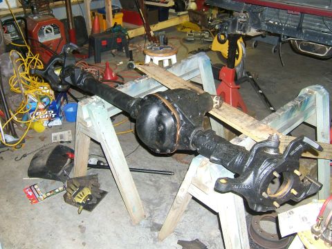 1993 Ford Bronco - A disassembled vehicle axle assembly is supported by sawhorses in a cluttered garage setting.