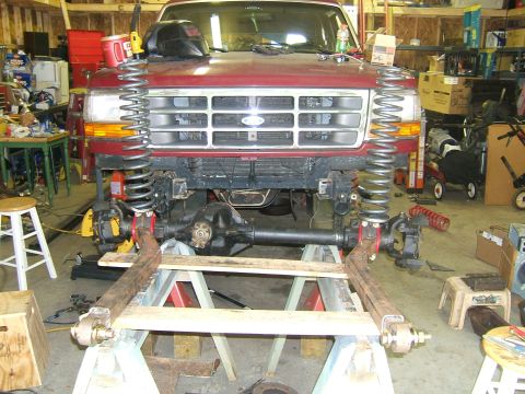 1993 Ford Bronco - A red 1993 Ford Bronco is shown in a garage with its front suspension disassembled and supported by jack stands.