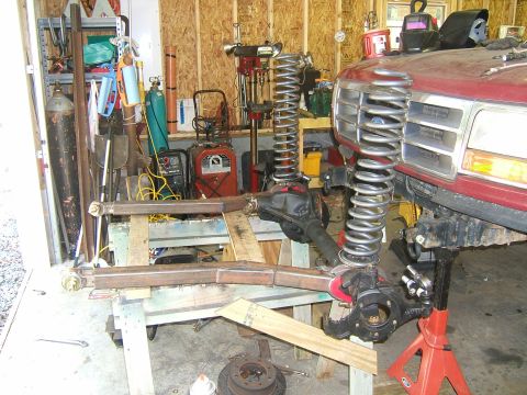 1993 Ford Bronco - Front end of a red Ford truck, likely from the early 90s, undergoing suspension modifications in a workshop.