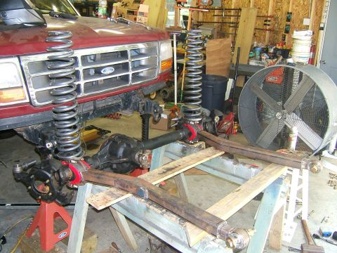 1993 Ford Bronco - Front suspension of a red Ford Bronco is disassembled for modification in a garage setting.