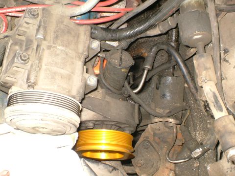 1989 Ford Bronco - Close-up of engine components, including a compressor and pulleys, with visible hoses and wiring.