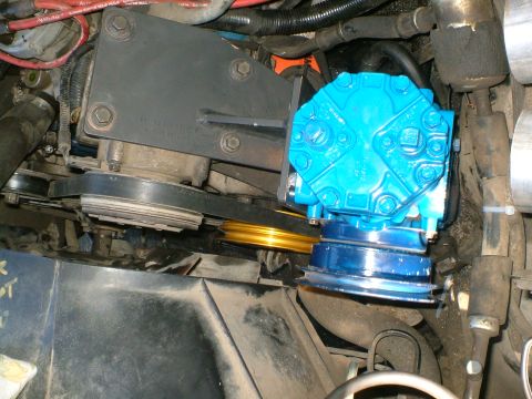 1989 Ford Bronco - Close-up of a blue compressor unit being installed with belts and pulleys.