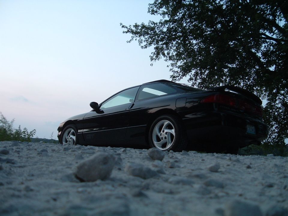 Black 1995 Ford Probe parked on a gravel surface with a tree overhead