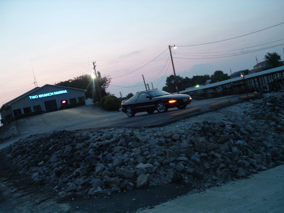 Black coupe driving on a road near a building labeled 'TWO BRANCH MARINA'
