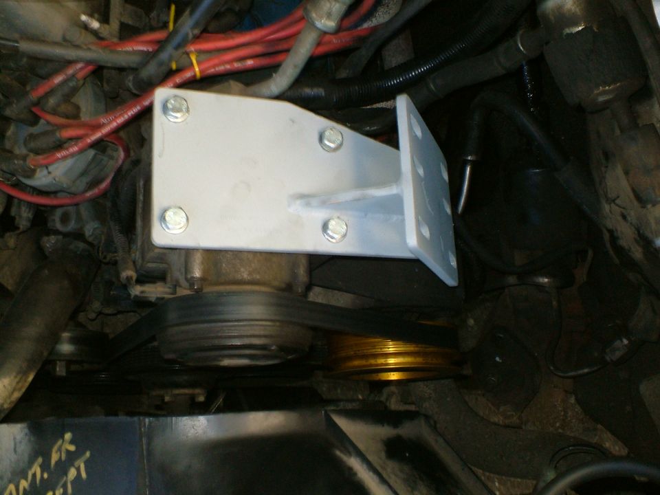 Engine compartment with a silver metal bracket bolted to a pulley system, red wires visible