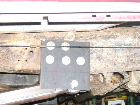 1993 Ford Bronco - Underside view of a heavily rusted vehicle frame with a bolted-on plate and cable.