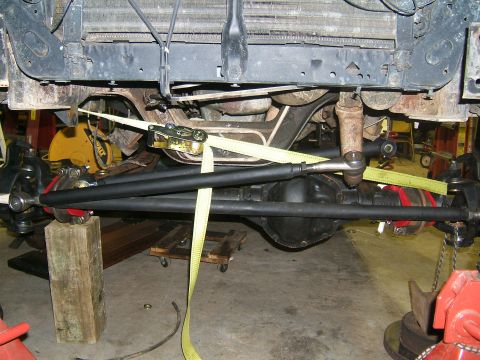 1993 Ford Bronco - The front axle and steering components of a vehicle are visible, secured with straps and blocks.